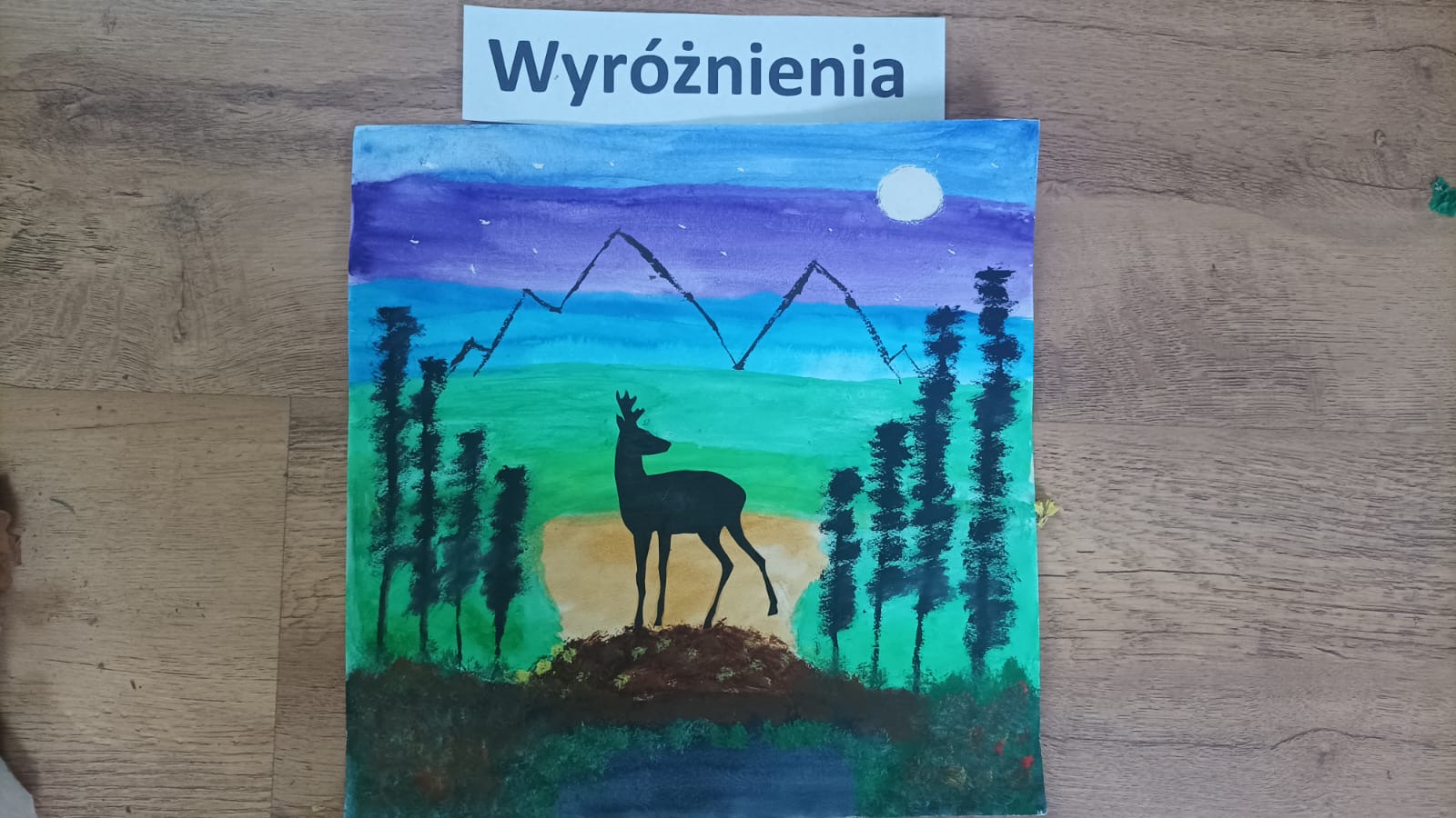 Wyróżnienie, namalowany obraz przedstawia jelenia w lesie na tle gór.