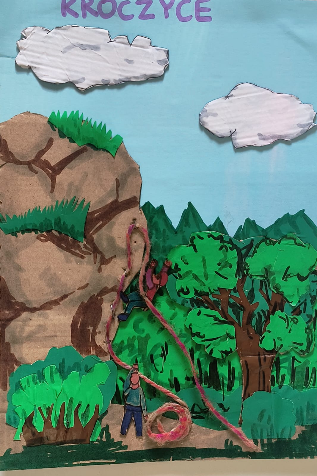 Dwóch mężczyzn wspina się na stromą skałę na tle zielonego lasu i błękitnego nieba z białymi chmurkami.