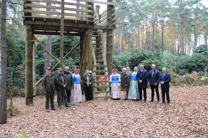 Pani Dyrektor ZPKWŚ, kierownik ZPKWŚ O/B w Kalinie i pozostali zaproszeni goście pozują do fotografii na tle wieży widokowej. 