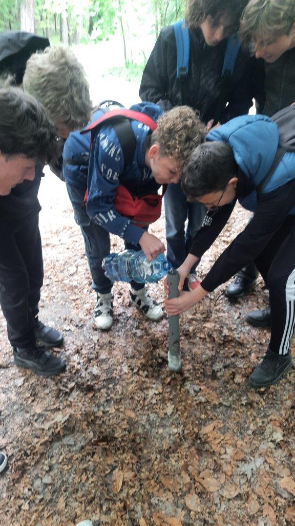 widać sześciu chłopców schylają się. Jeden trzyma rurkę a drugi wlewa z bańki do rurki wodę. 