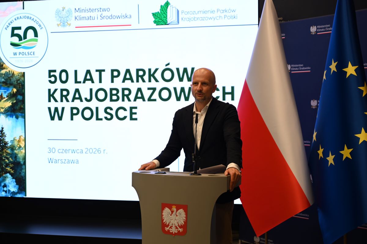 Główny Konserwator Przyrody Mikołaj Dorożała stoi przy mównicy i przemawia do zgromadzonych uczestników konferencji 50 – lecia parków krajobrazowych. W tle napis 50 – lecie parków krajobrazowych.
