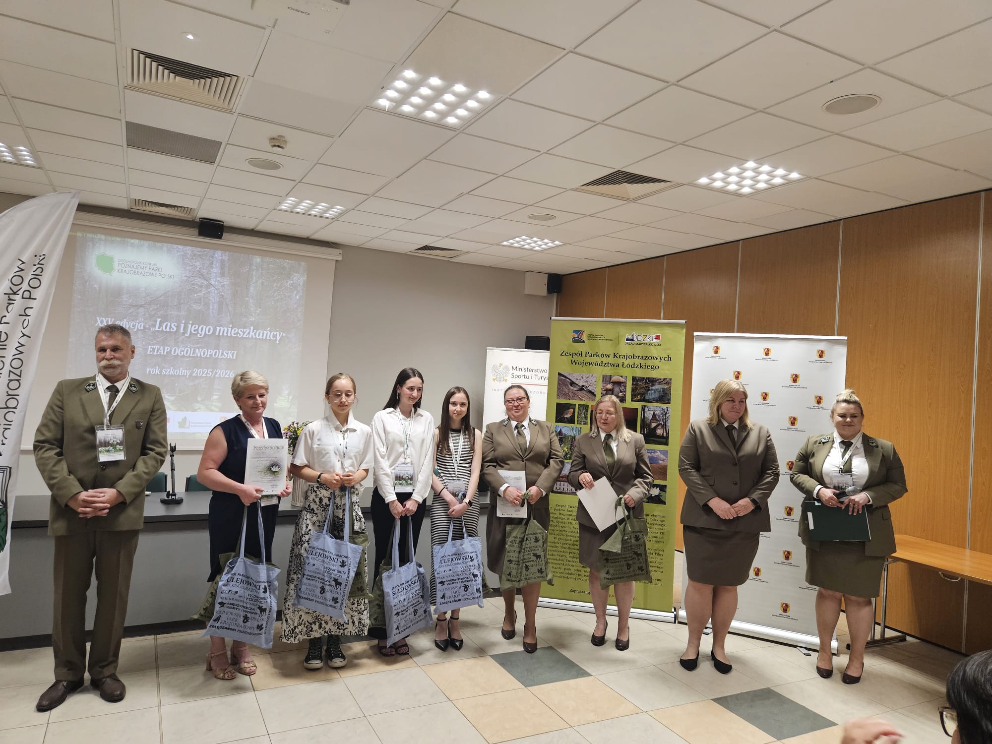 9nsoób pozuje do zdjęcia z dyplomami i nagrodami. 5 osób w mundurach - przedsatawiciele Parków Krajobrazowych. 4 osoby - drużyna reprezentująca województwo śląskie