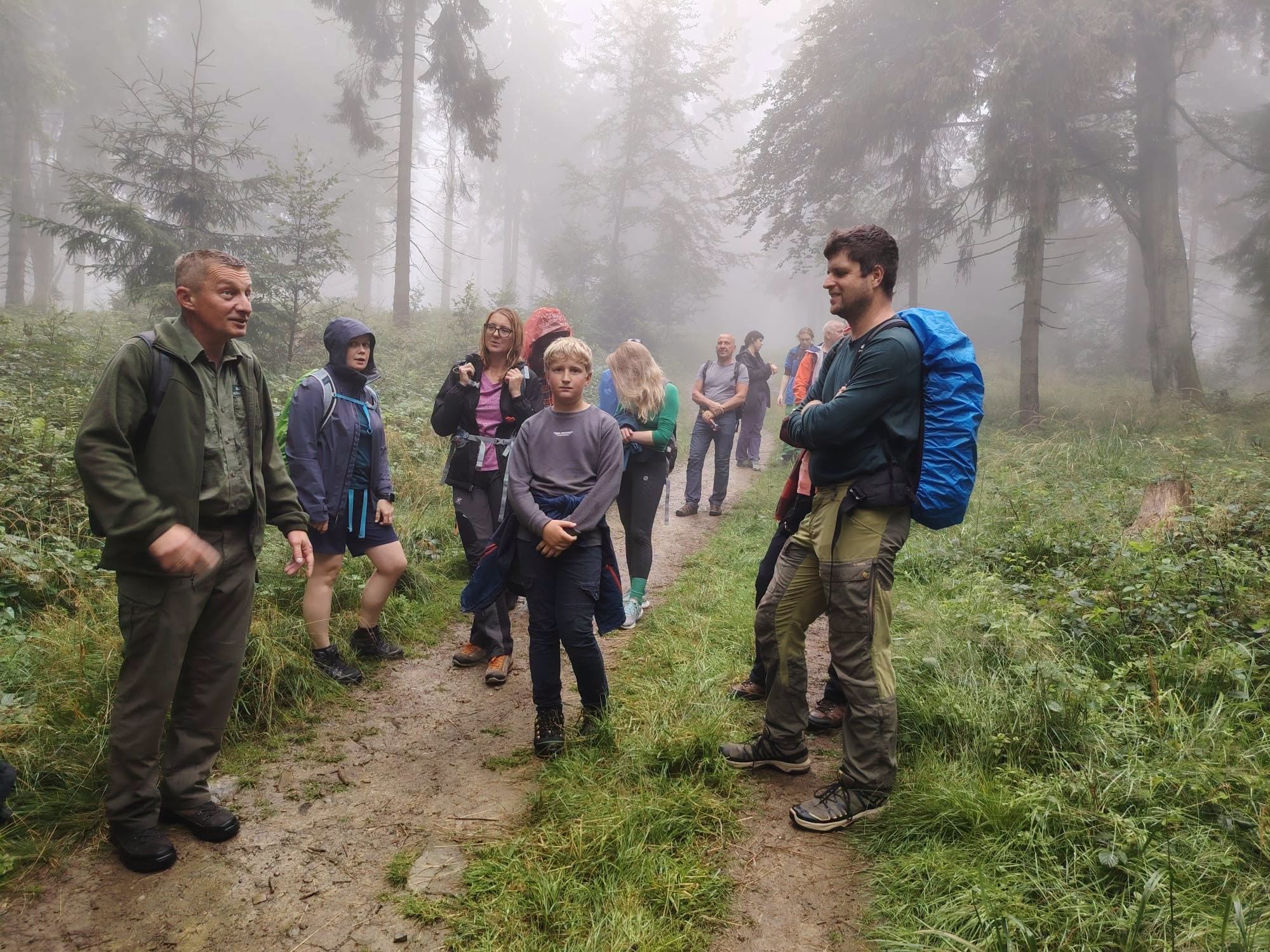 Grupa osób stoi w lesie i rozmawia.